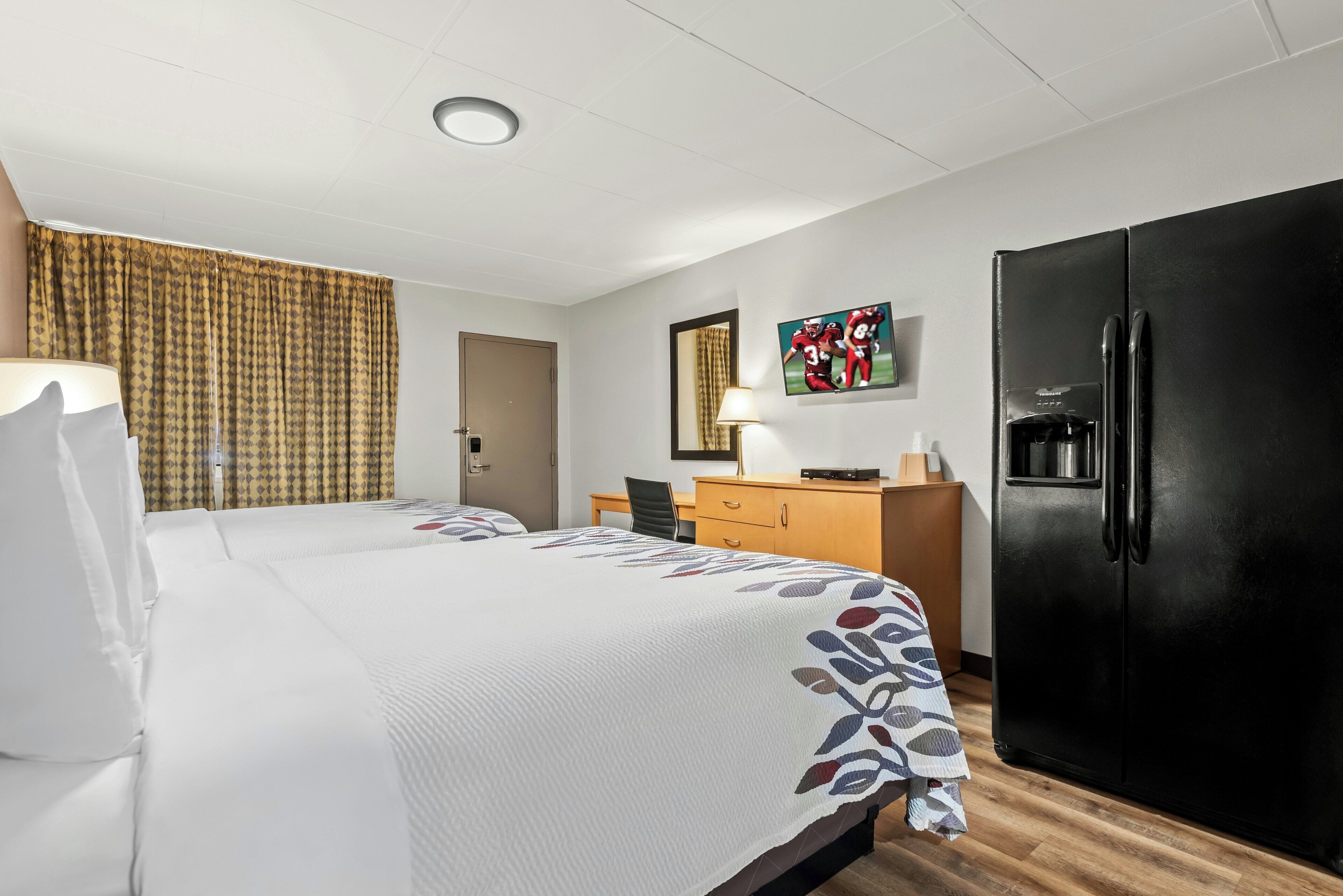 Une chambre d’hôtel équipée d’un lit, d’un bureau, d’un réfrigérateur et d’une télévision.