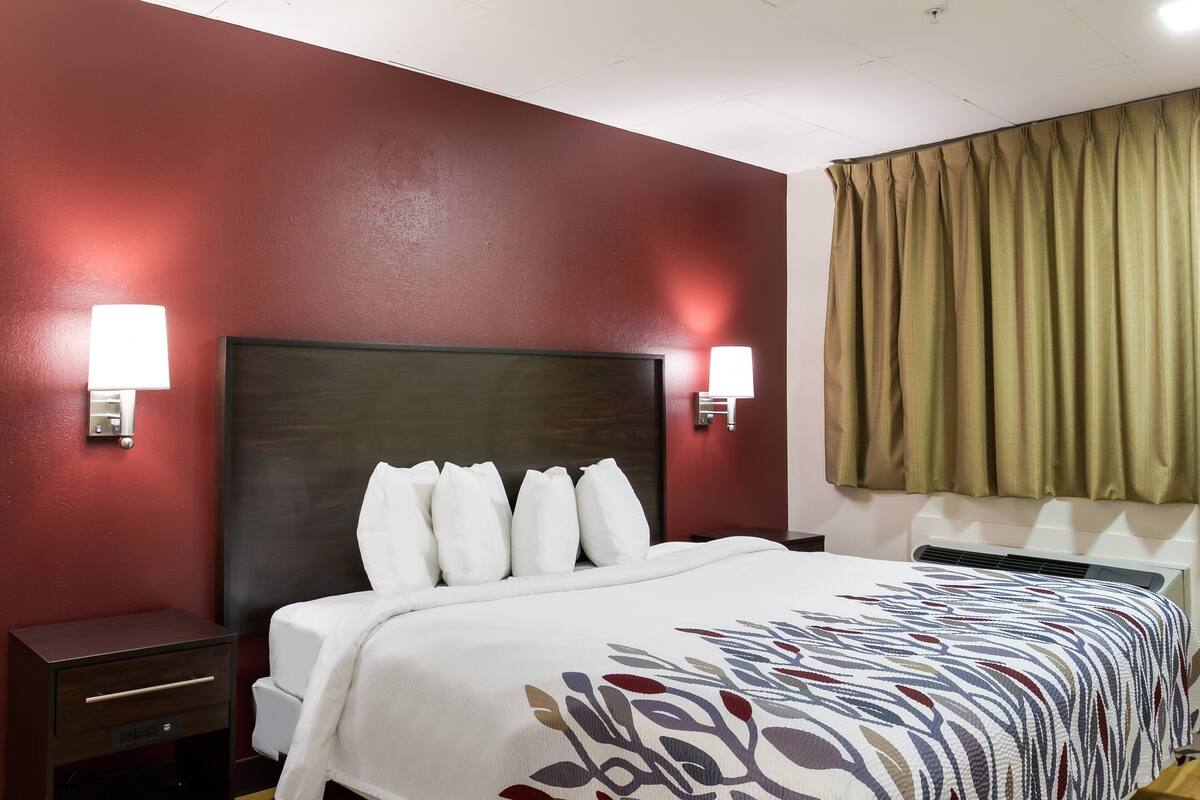 A hotel room with a dark headboard, white bedding, two bedside lamps, and a window with curtains.