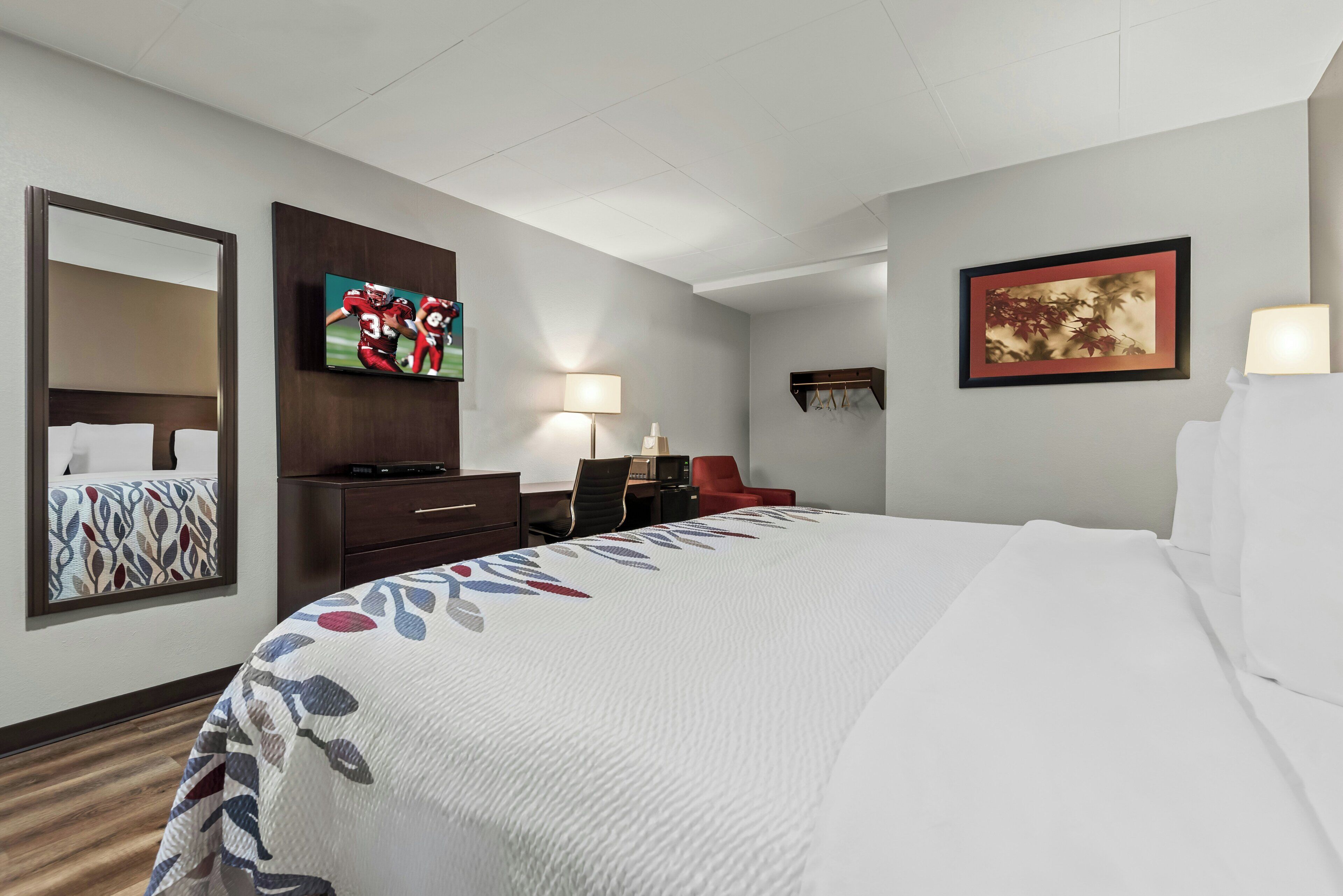 Habitación de hotel con cama, escritorio, silla, televisor, lámpara y obras de arte en las paredes.