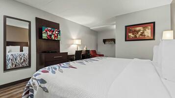 Habitación de hotel con cama, escritorio, silla, televisor, lámpara y obras de arte en las paredes.