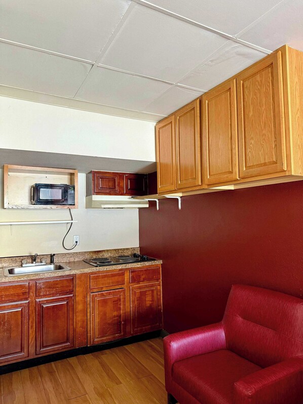 A compact kitchen with wooden cabinets, a microwave, a stove, and a red chair.