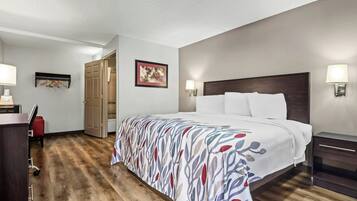 A hotel room with a bed, bedside lamps, a desk with a chair, a wardrobe, and a door leading to a bathroom.
