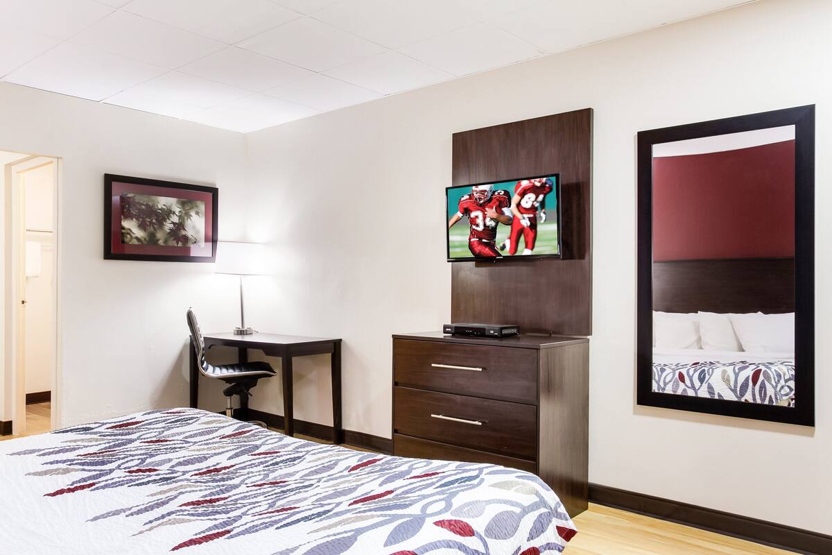 A hotel room with a bed, a desk, a TV, and a large mirror.
