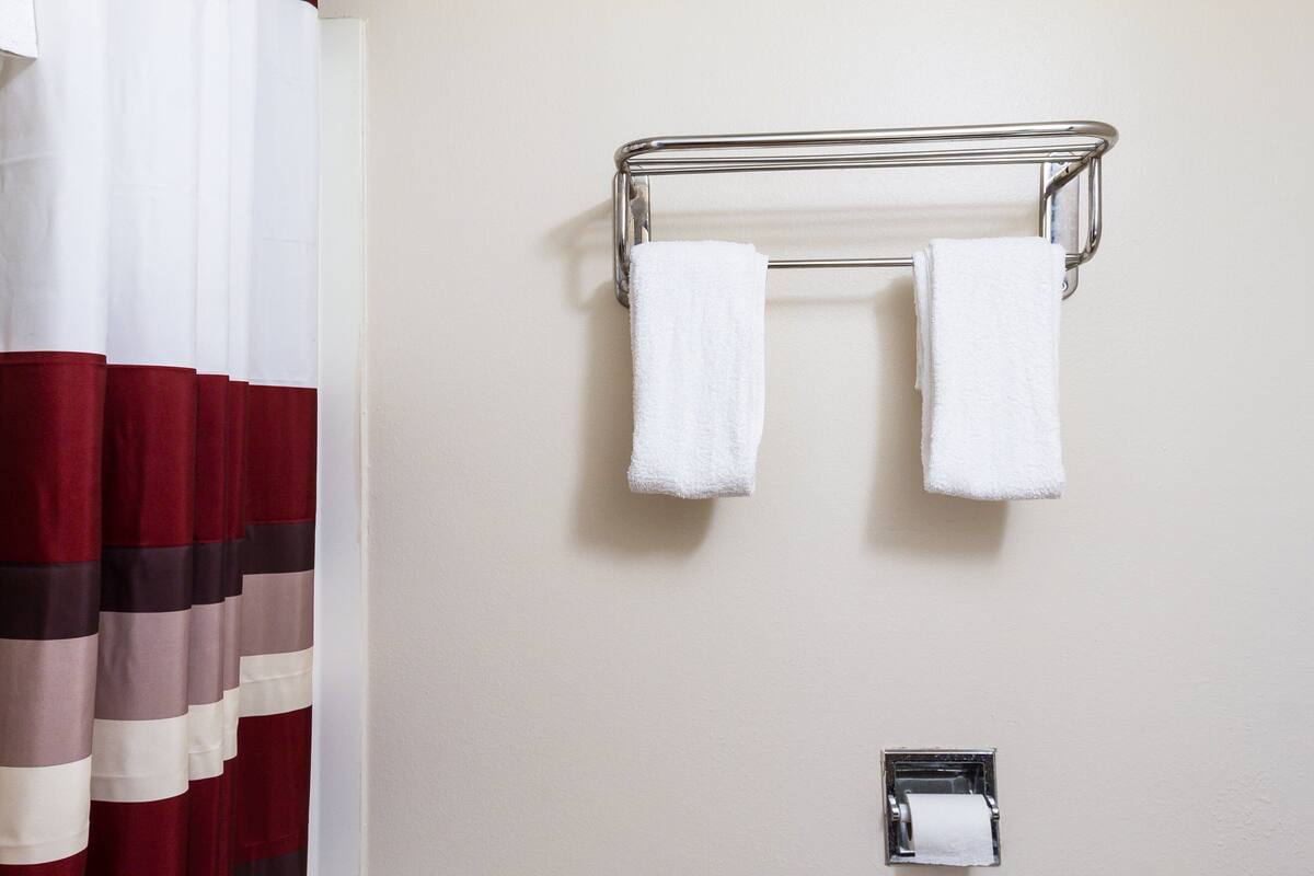 A bathroom with a towel rack holding two white towels, a toilet paper holder, and a striped curtain.