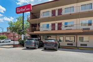 A multi-story motel with a Red Roof Inn sign, two parked cars, and a clear sky.