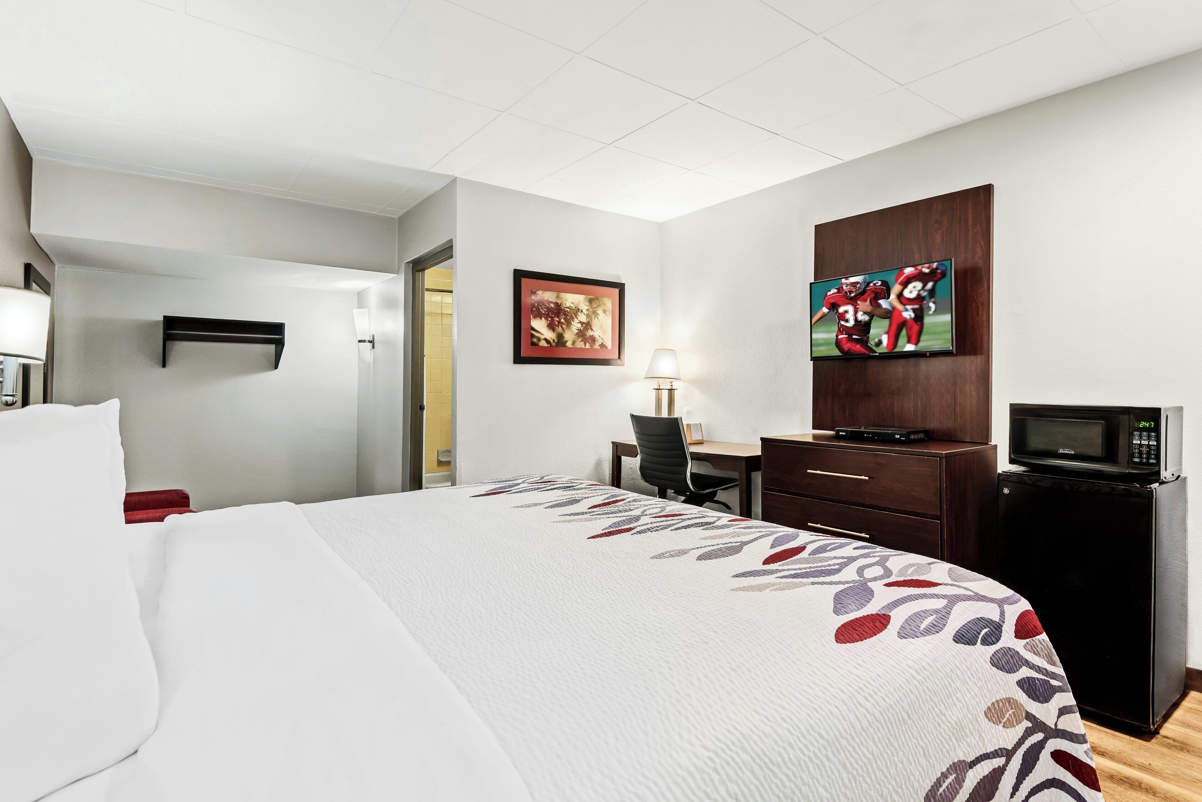 A hotel room with a bed, a desk, a television, and a microwave.
