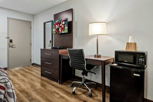 A hotel room with a desk, chair, TV, lamp, microwave, and a door with a lock.