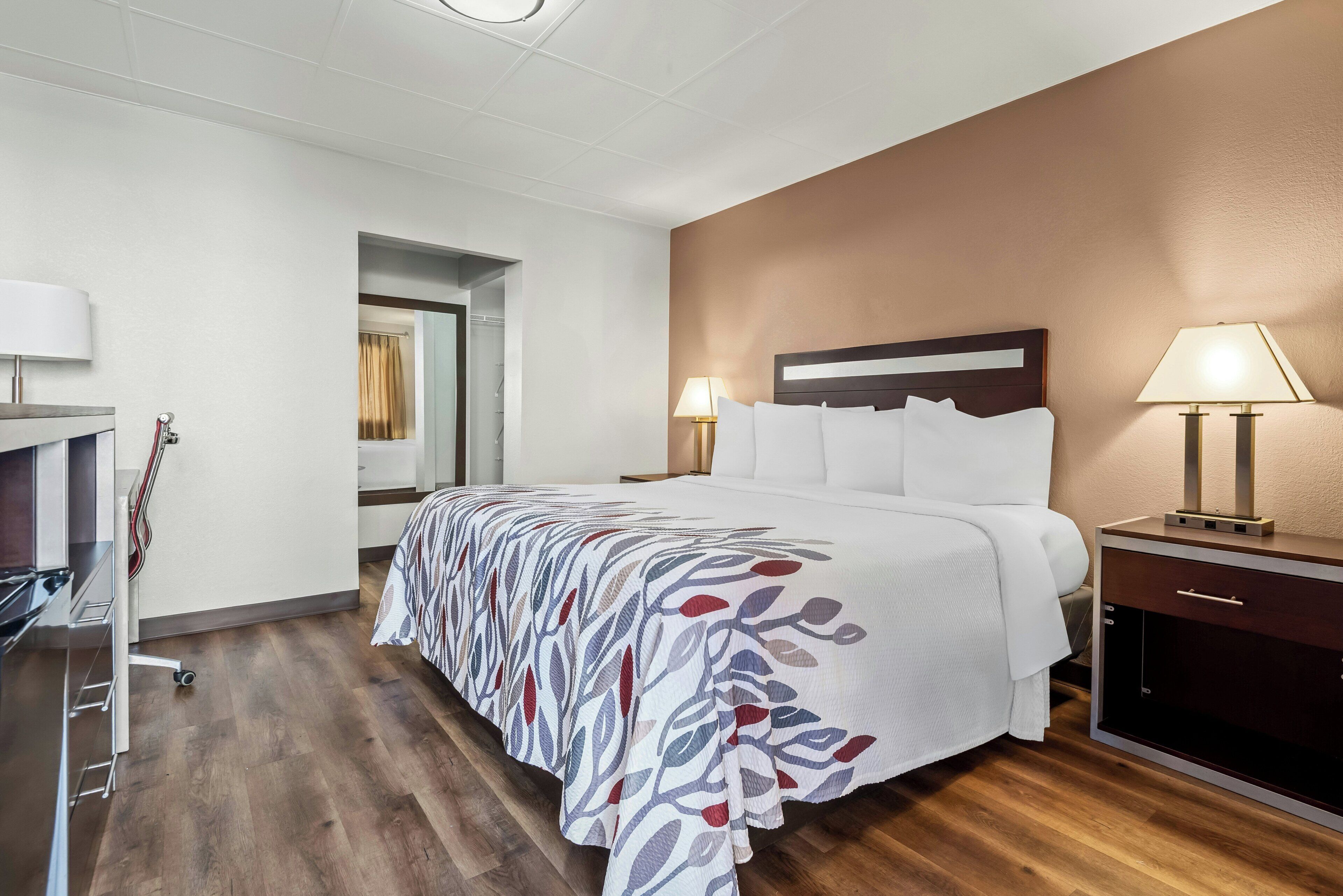 A hotel room with a bed, bedside lamps, a wardrobe, a desk, and a mirror.