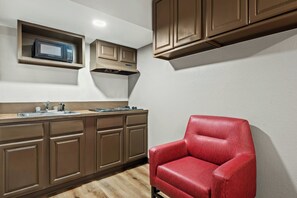 A compact kitchen with a built-in microwave, stove, and cabinets, and a red leather chair in the corner. - Red Roof Inn York Downtown (York)