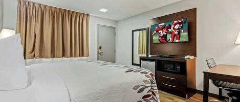 Una habitación de hotel con cama, escritorio, televisor y armario.