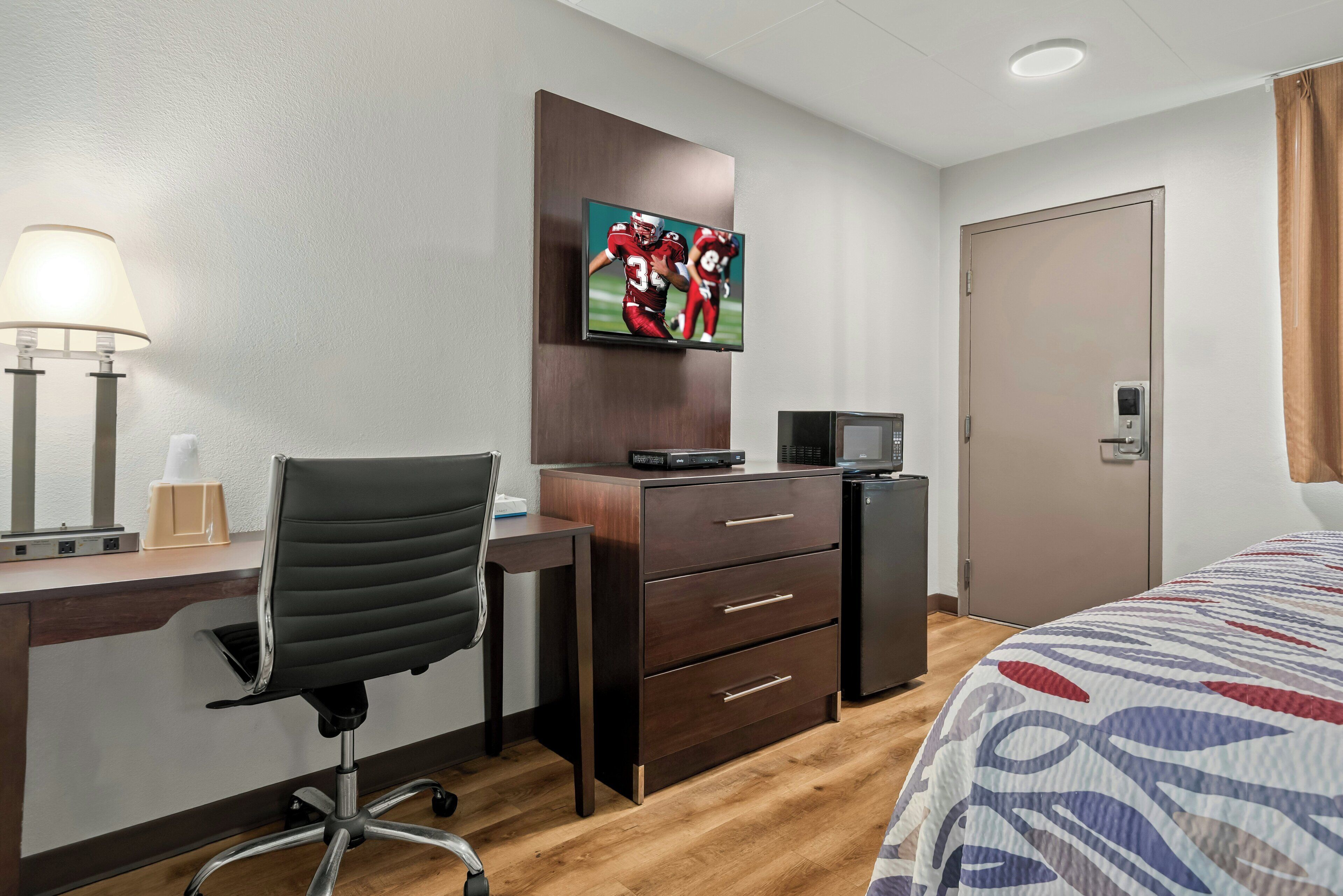 A hotel room with a desk, chair, television, and a bed.