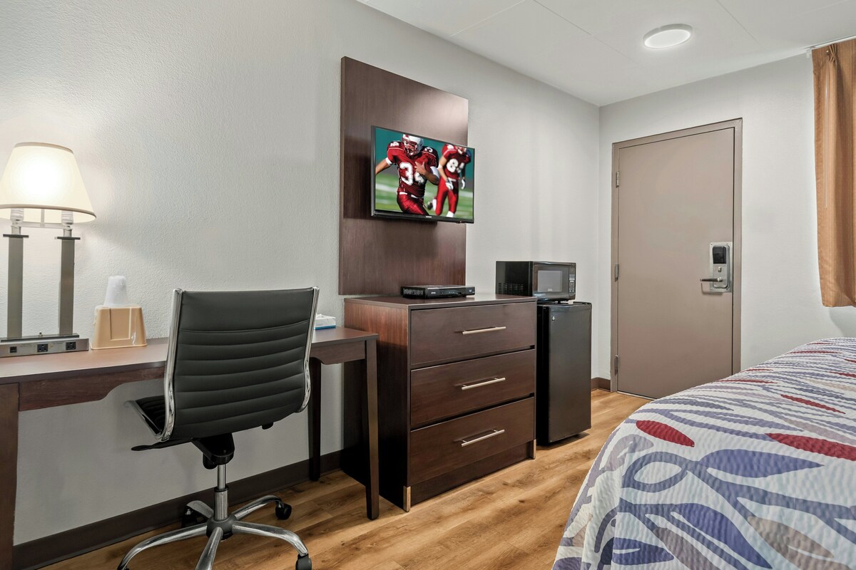 Ein Hotelzimmer mit Schreibtisch, Stuhl, Fernseher und einem Bett.