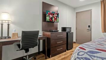 A hotel room with a desk, chair, television, and a bed.