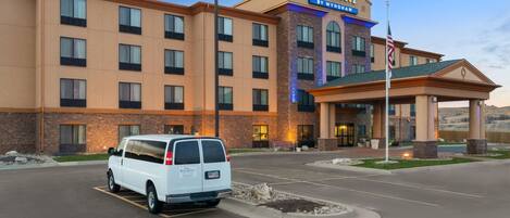Un hotel Baymont by Wyndham con una camioneta blanca estacionada frente a él, una entrada bien iluminada y una bandera en el asta.