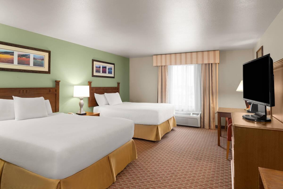 Een hotelkamer met twee bedden, een bureau, een televisie en een raam met gordijnen.
