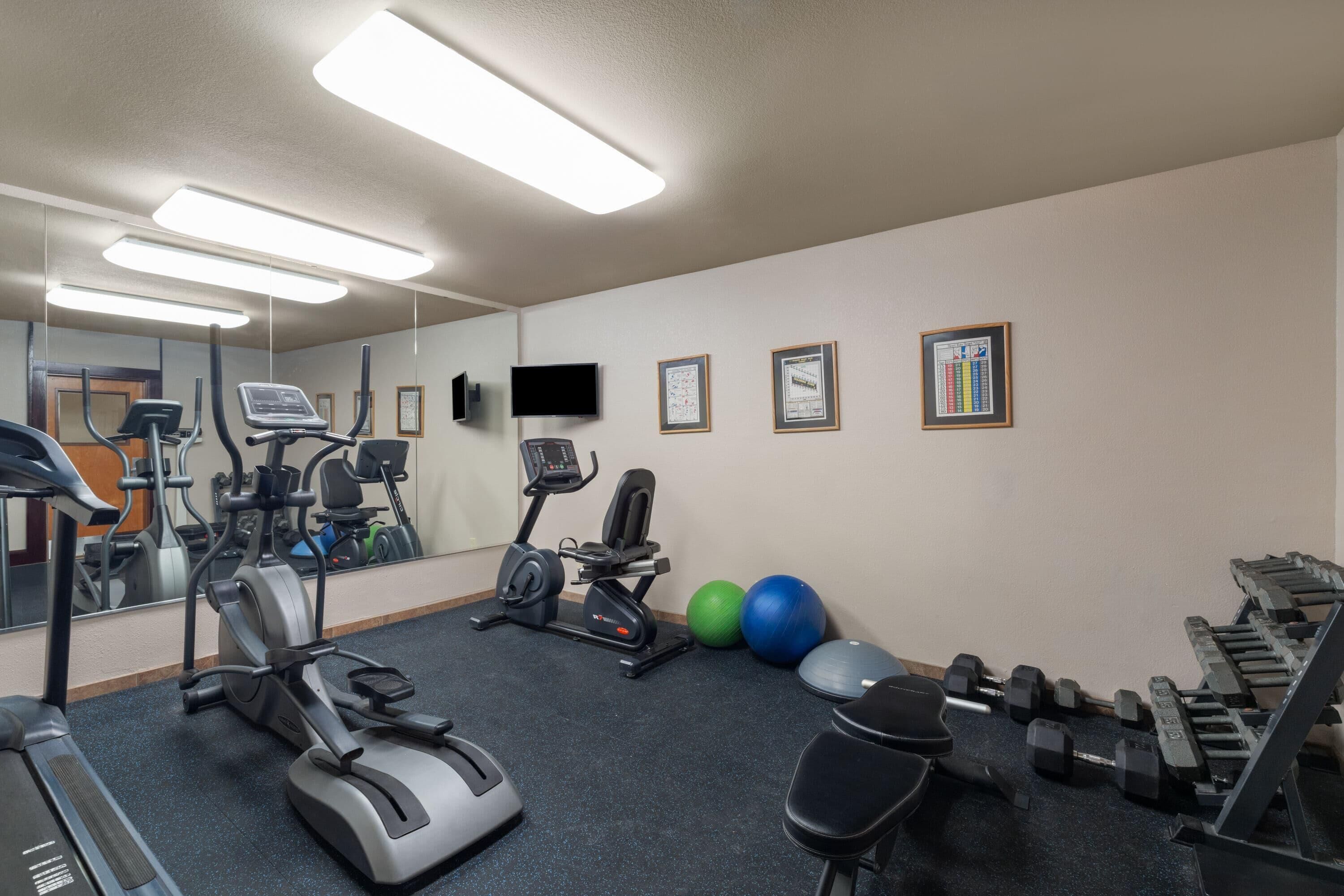 Un gimnasio con cintas de correr, elípticas, bicicletas estáticas y pesas libres.