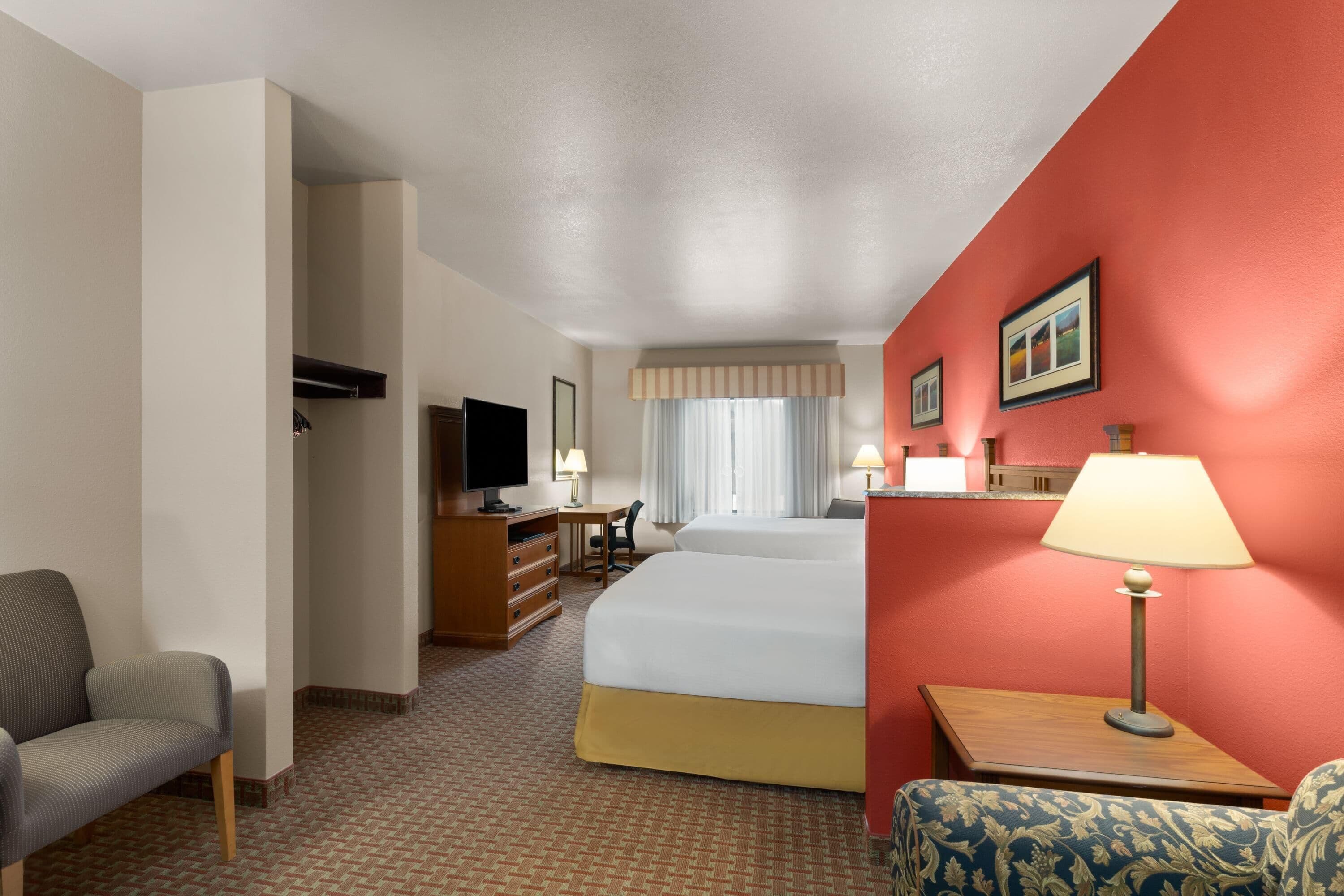 A hotel room with a bed, a desk, a chair, a TV, and a lamp.