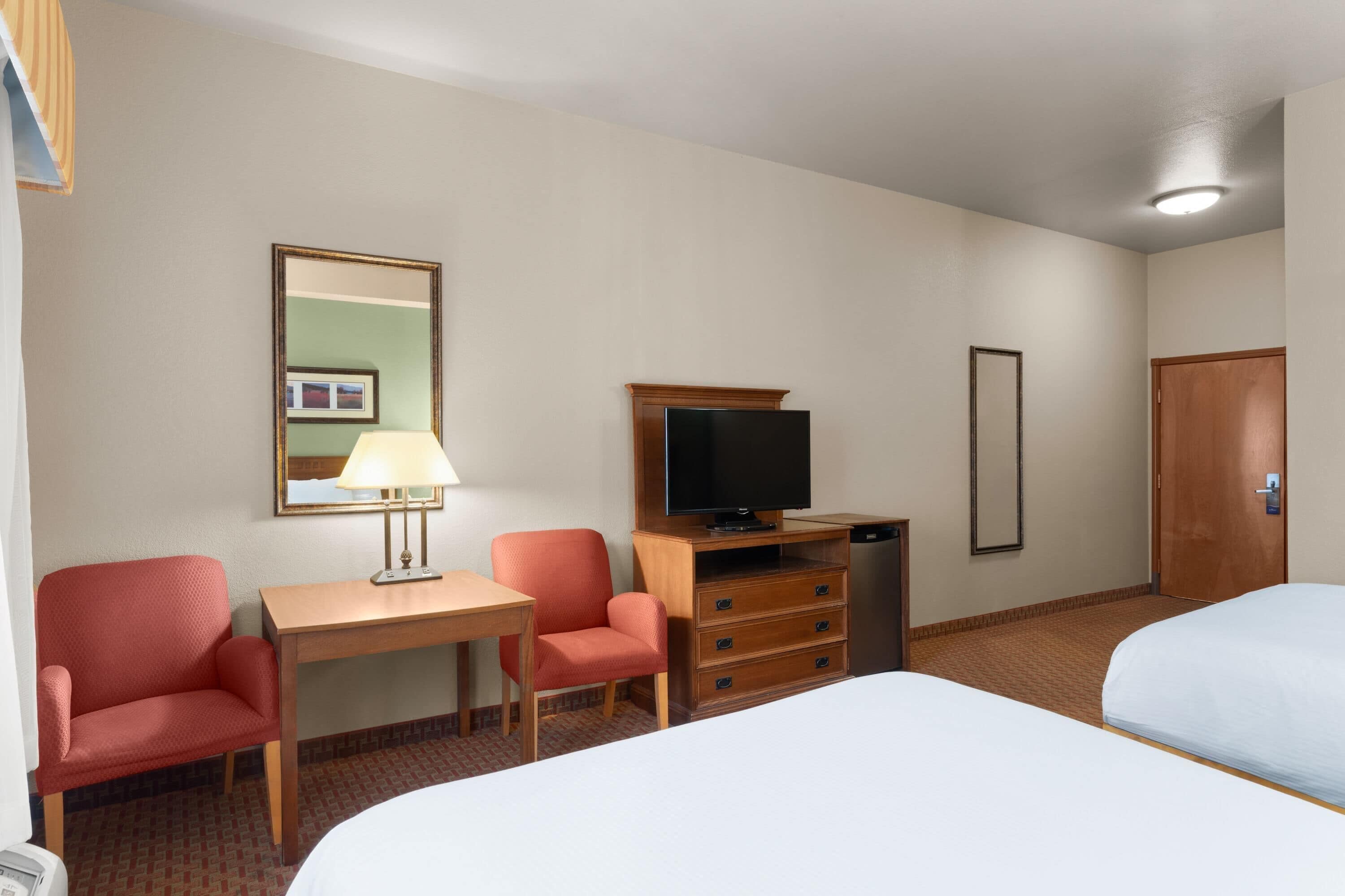 Una habitación de hotel con dos camas, un escritorio con lámpara, televisión, cómoda y una puerta.
