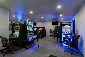 A gaming room with multiple arcade machines, chairs, and a television screen. - Baymont Inn and Suites by Wyndham Sturgis (Sturgis)
