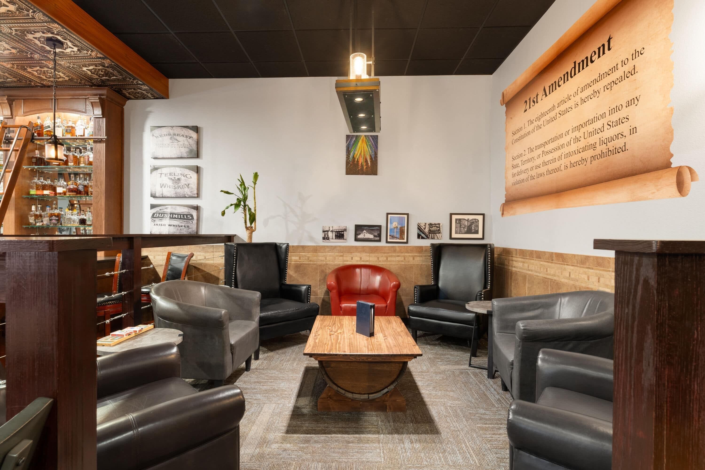 Cómoda sala de estar con asientos de cuero, una mesa de centro de madera y una pared grande que muestra el texto de la 21ª Enmienda.