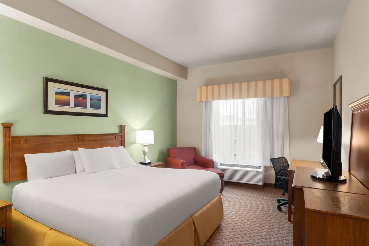 Een hotelkamer met een groot bed, een bureau met computer, een stoel, een televisietoestel en een raam met gordijnen.