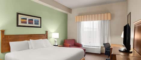 A hotel room with a large bed, a desk with a computer, a chair, a television, and a window with curtains.