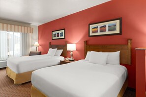 A hotel room with two beds, a window with curtains, a nightstand with a lamp, and two framed pictures on the wall. - Baymont Inn and Suites by Wyndham Sturgis (Sturgis)