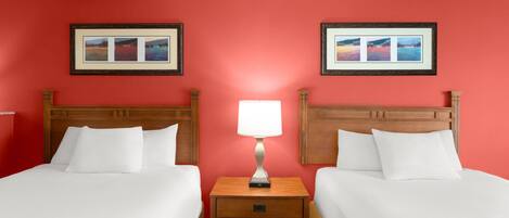 A hotel room with two beds, a nightstand with a lamp, and two framed pictures on the wall.