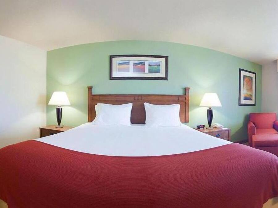 A hotel room with a large bed, two bedside tables with lamps, a chair, and a framed picture on the wall.