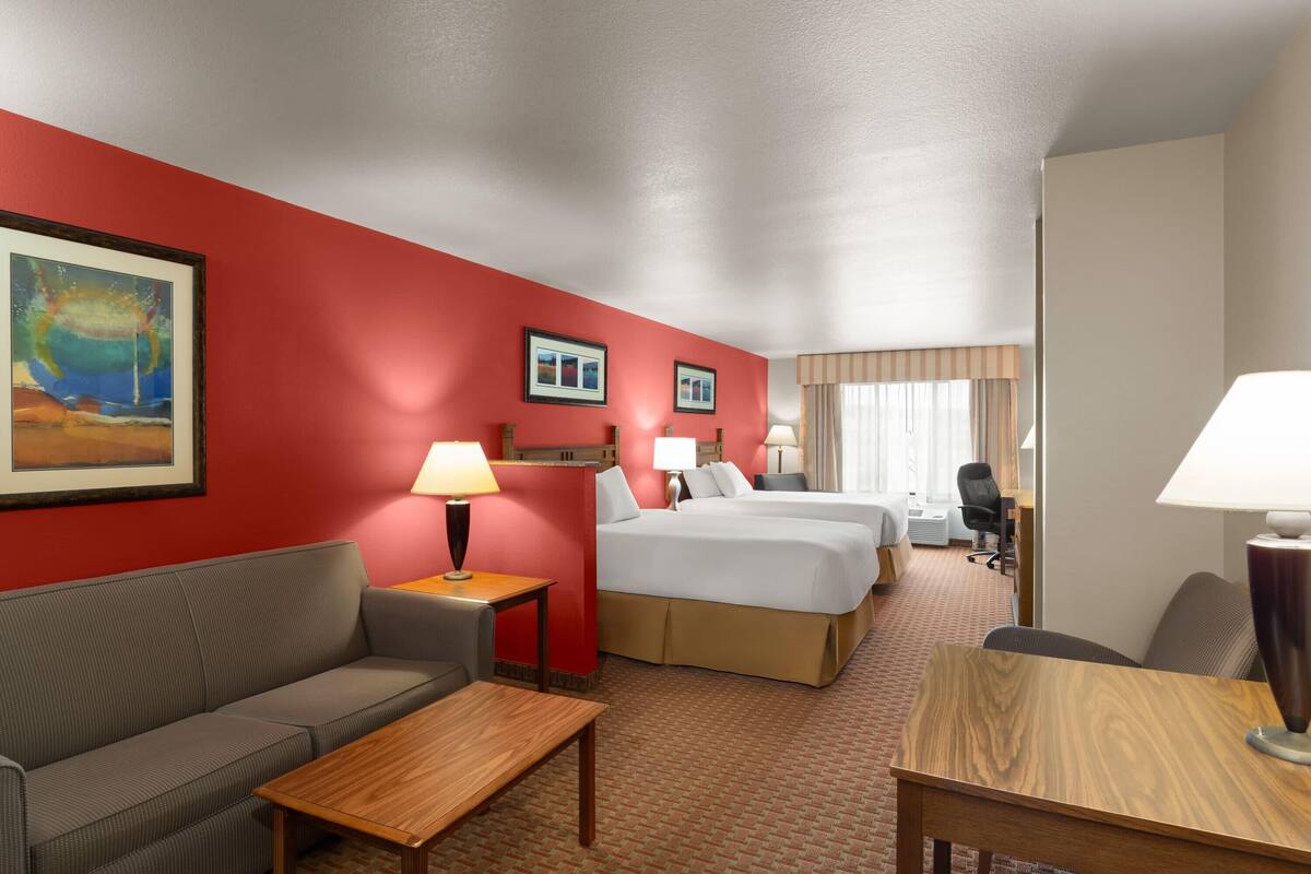 Een hotelkamer met een rode accentmuur, een bank, een bed, een bureau en een stoel.