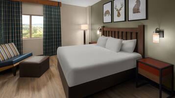 A hotel room with a large bed, a nightstand with a lamp, a bench, and a window with curtains.
