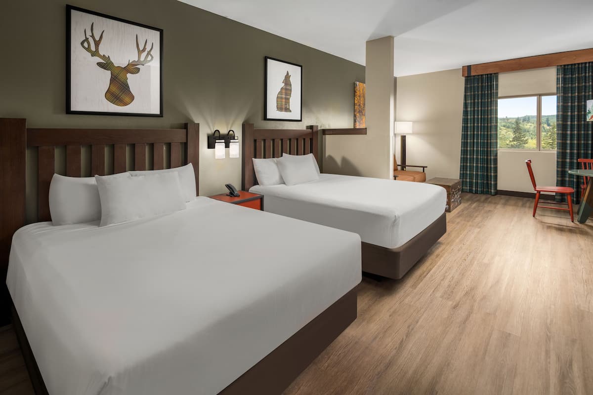 Habitación de hotel con dos camas, cabecera de madera, mesita de noche con lámpara, una silla y ventana con cortinas.