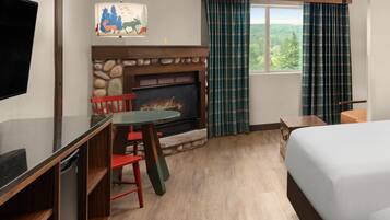 Una habitación de hotel con chimenea de piedra, una mesa de comedor con sillas, una cama y un ventanal con cortinas.