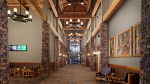 A lobby with a high ceiling, wooden beams, stone pillars, and a patterned carpet. There are seating areas with wooden furniture and artwork on the walls. - Great Wolf Lodge Grand Mound (Centralia)