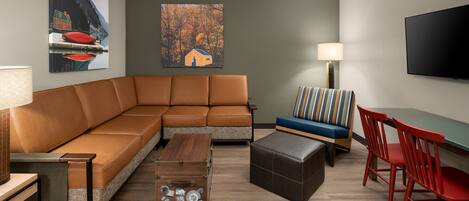 A modern living room with a sectional sofa, a small table, a blue sofa with striped cushions, a red chair, and a flat-screen TV mounted on the wall.