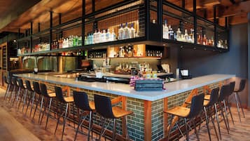 A bar area with a long counter, multiple stools, and shelves stocked with bottles.