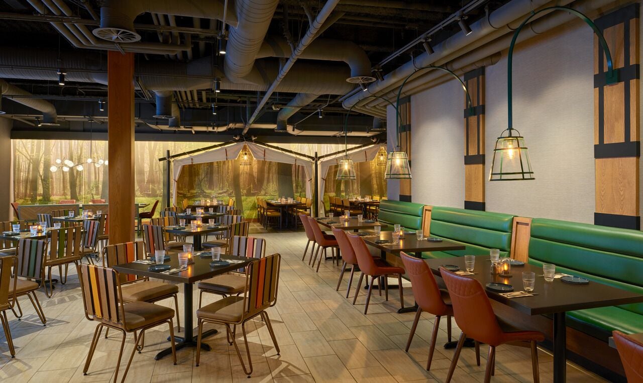 A restaurant interior with tables and chairs, a green booth, and pendant lighting.