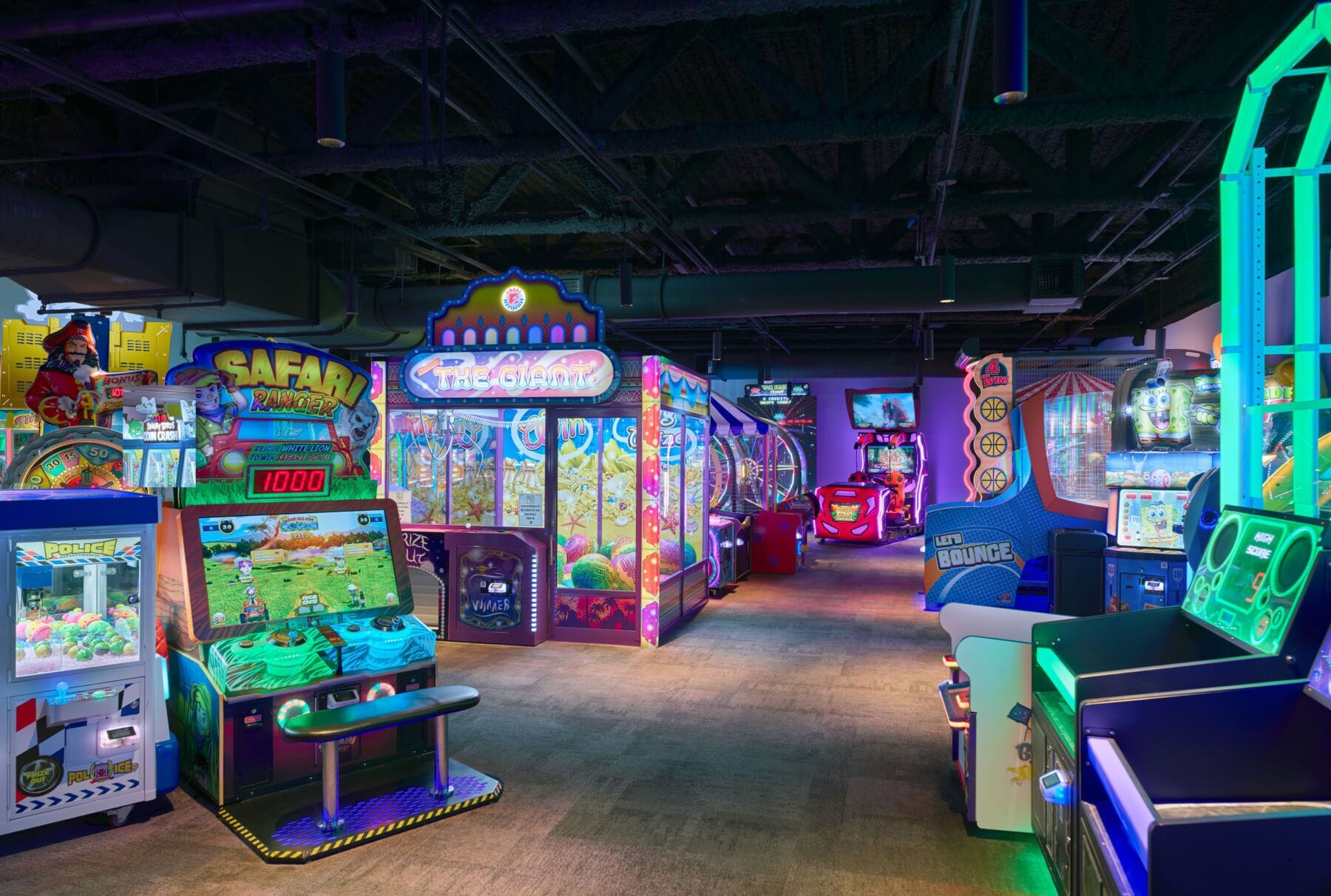 Un salón de juegos interior con diversas máquinas recreativas, incluidas máquinas de garra y juegos de carreras.