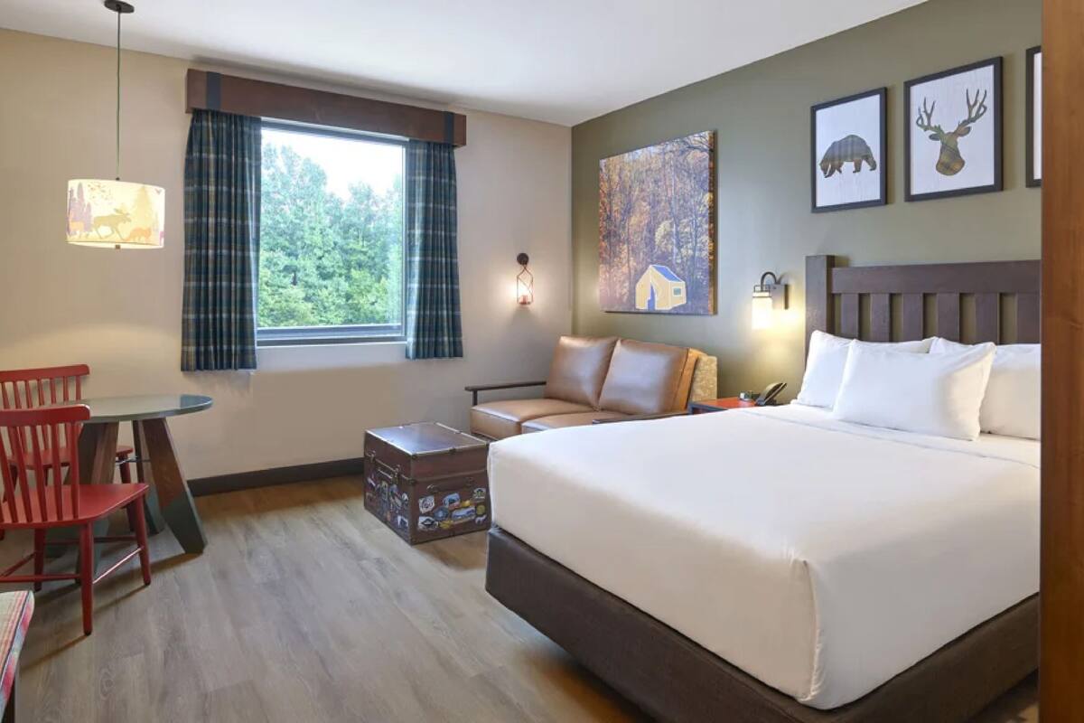 Habitación de hotel con una cama grande, un escritorio con silla, una ventana con cortinas y decoración en la pared.