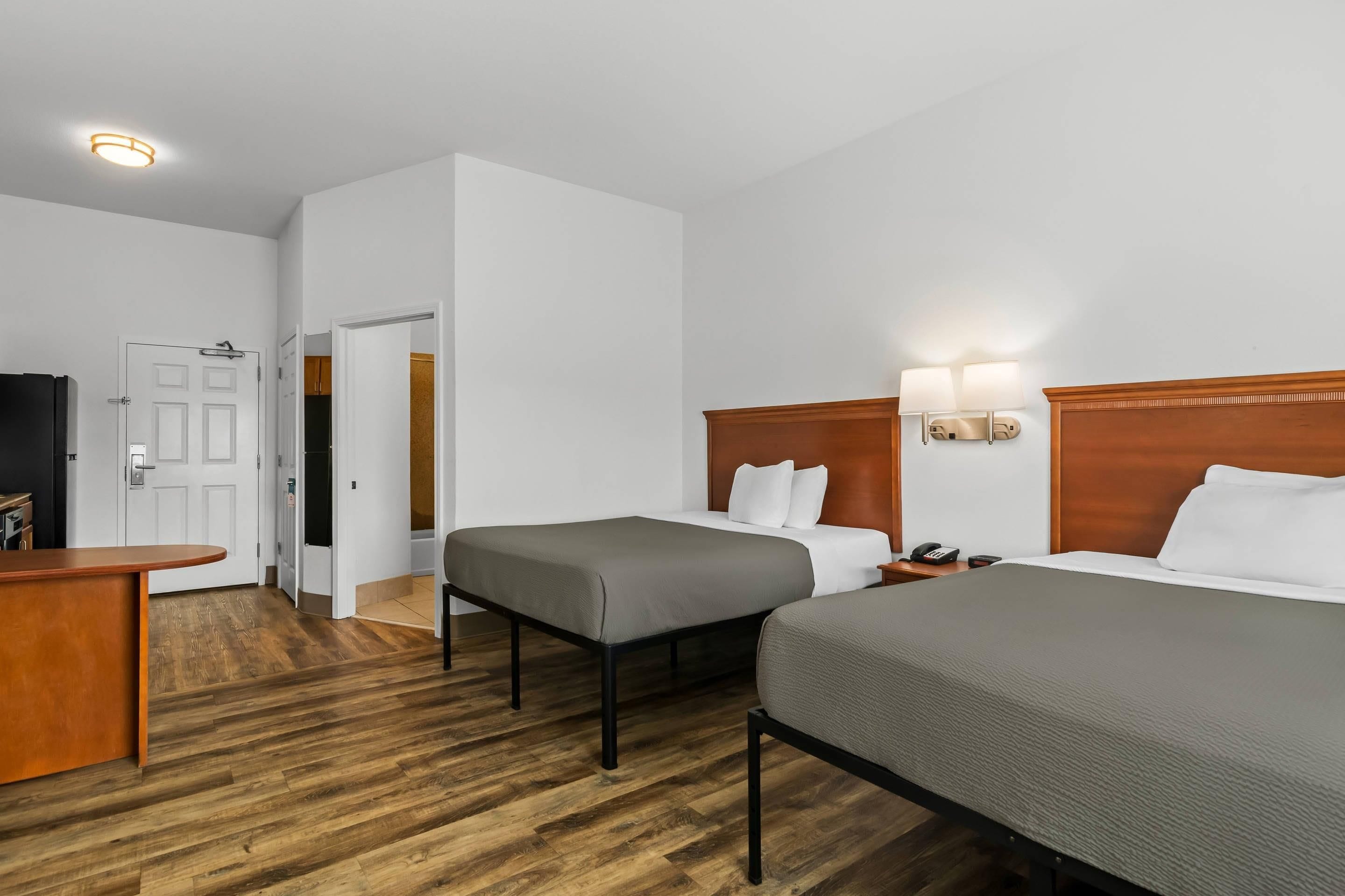 Quarto de hotel com duas camas, uma escrivaninha, um guarda-roupa e um banheiro visível através de uma porta aberta.