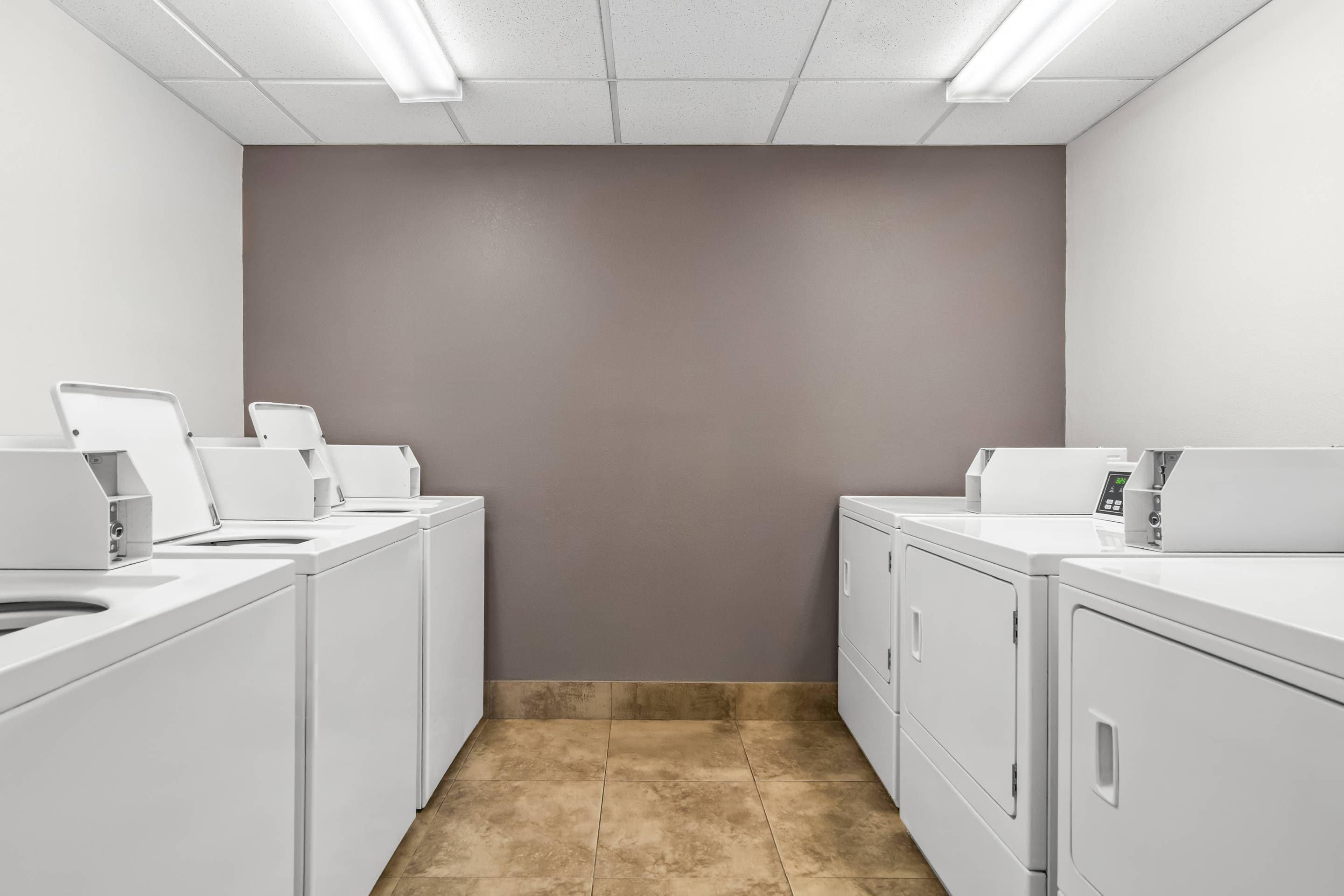 A laundry room with two washing machines, a dryer, and a control panel.
