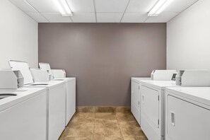 A laundry room with two washing machines, a dryer, and a control panel. - Suburban Studios Fort Smith (Fort Smith)