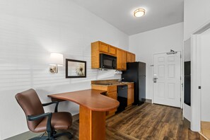 Una cocina compacta con armarios de madera, un microondas, un refrigerador y una zona de comedor con mesa y sillas.