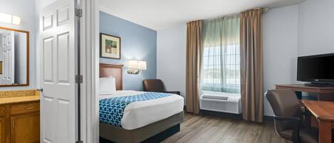 A hotel room with a bed, desk, chair, television, and a window with curtains.