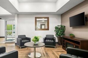 A modern waiting area with leather chairs, a round table, a mirror, and a TV on the wall. - Suburban Studios Fort Smith (Fort Smith)