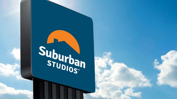 A sign for Suburban Studios with a clear blue sky and clouds in the background.