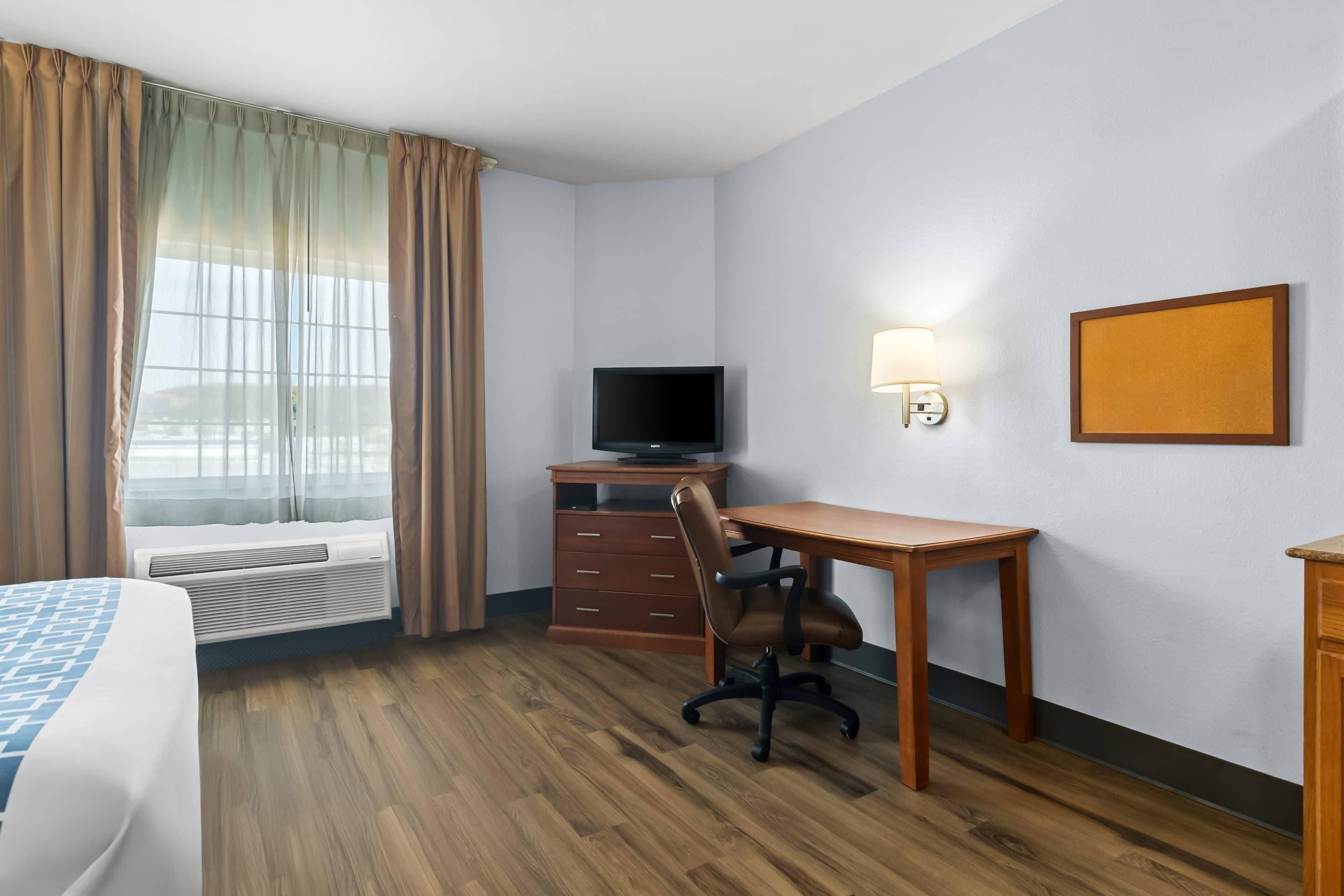 A hotel room with a bed, a desk, a chair, a television, and a wall-mounted lamp.