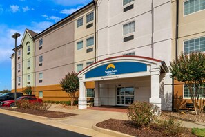 A Suburban Studios hotel with a modern facade, multiple windows, and a parking lot with cars. - Suburban Studios Fort Smith (Fort Smith)
