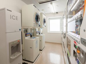 A laundry facility with washers and dryers, a vending machine, and a window providing natural light. - Comfort Hotel Kitami (Kitami)