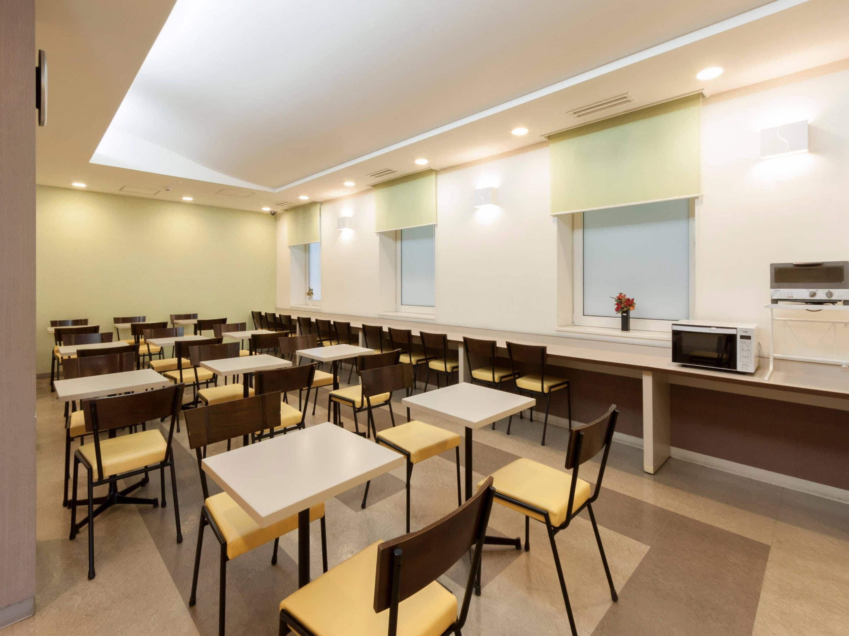 A cafeteria with multiple tables and chairs, a microwave, and a window with a view.